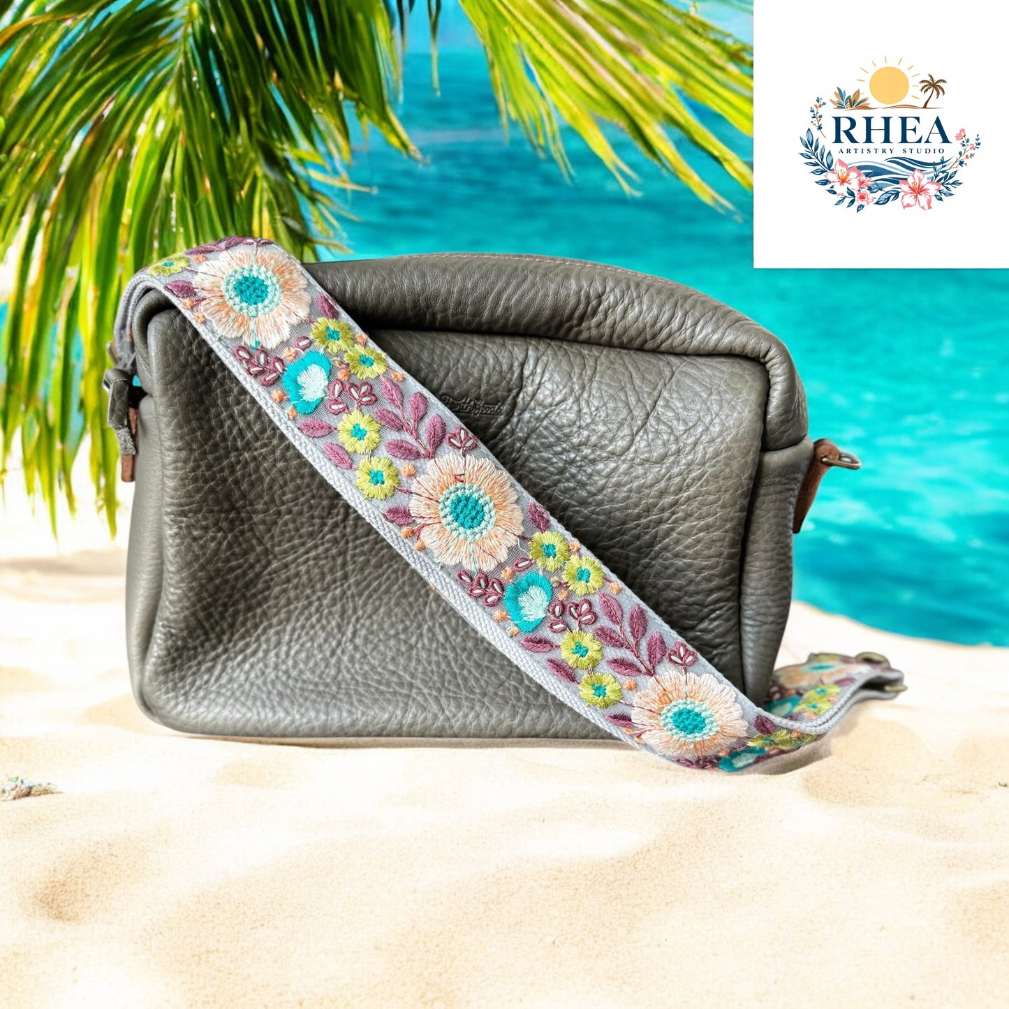 A taupe handbag with a floral strap featuring aqua, coral, and lavender embroidery. Set in a beach