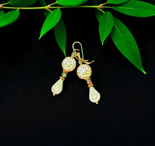 Gold earrings with gemstones on a black background with green leaves