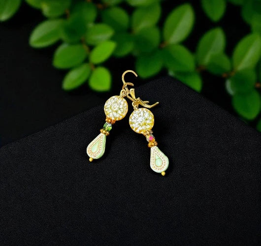 Gold earrings with gemstones on a black surface with green leaves in the background
