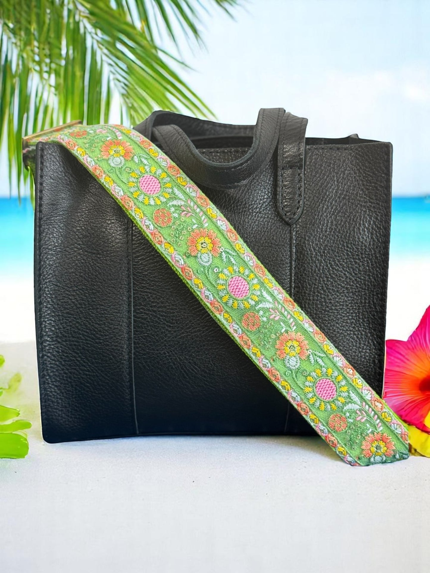 Embroidered green daisy strap styled with a black tote on a beach backdrop.