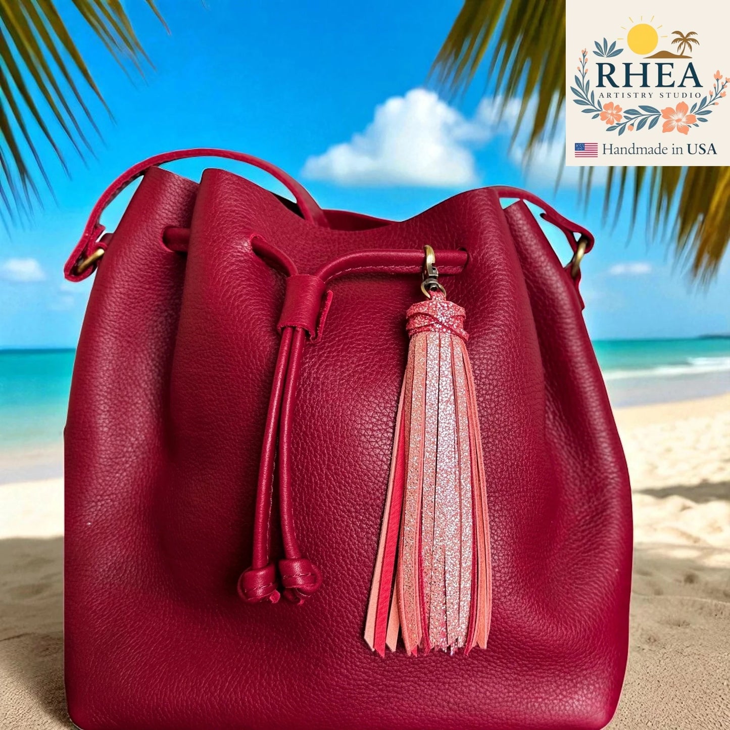 Red leather bucket bag with a tassel on a beach background, featuring the RHEA brand.