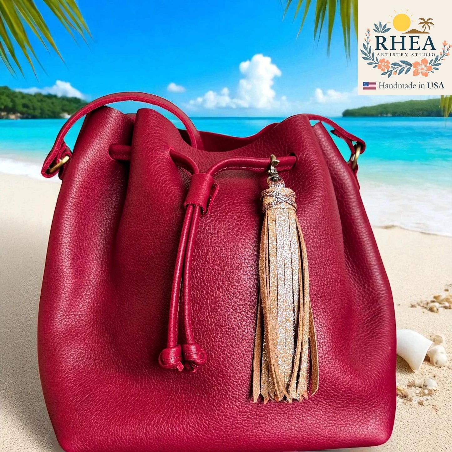 Red leather bucket bag with a tassel on a beach, featuring the RHEA brand.