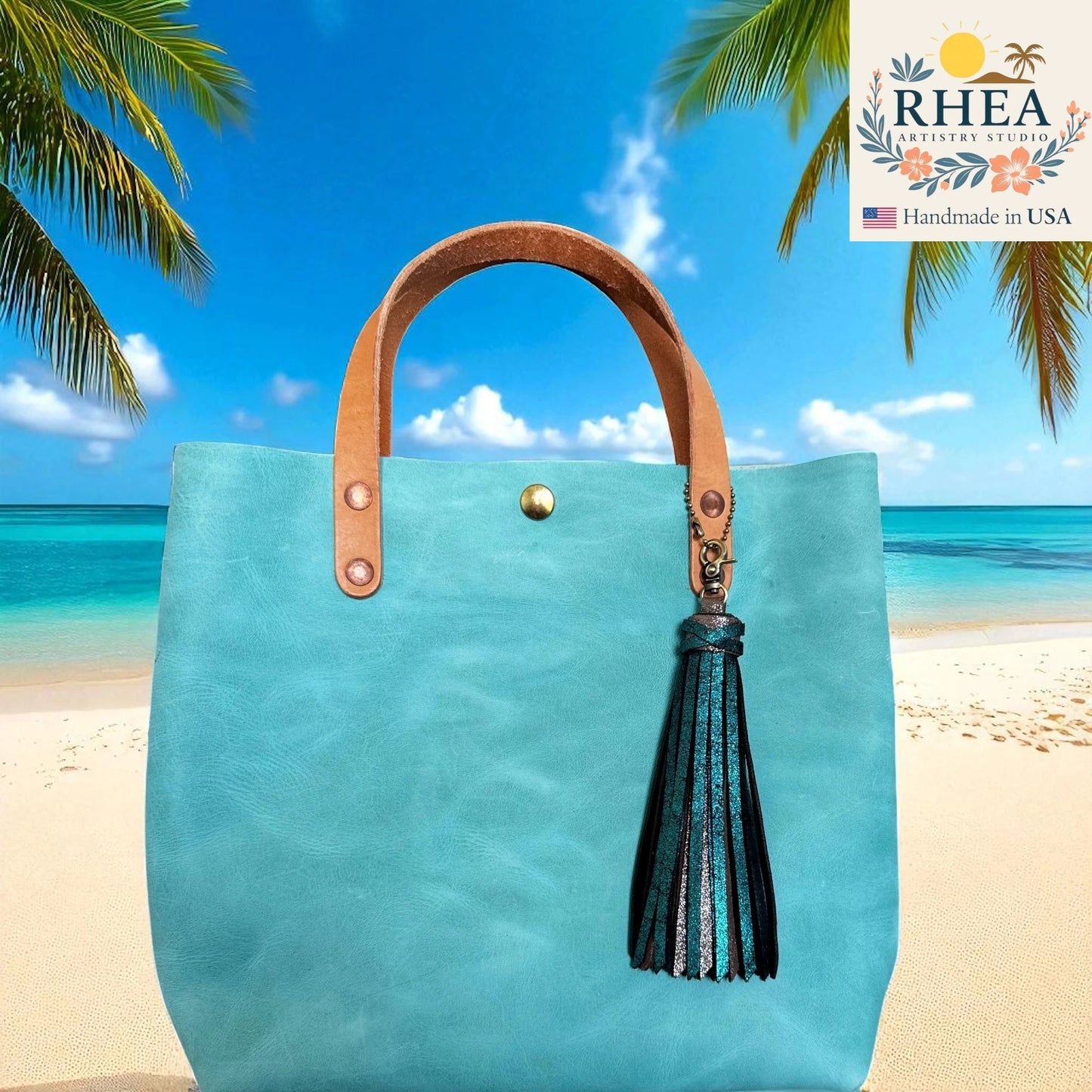 Turquoise tote bag with brown handle and tassel on a beach background, featuring RHEA branding.