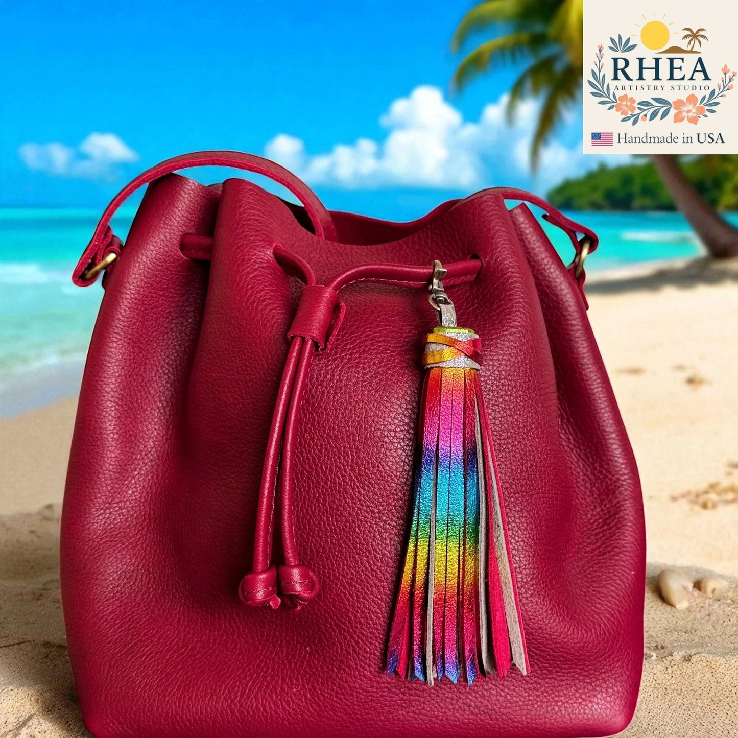 Red leather bucket bag with a colorful tassel on a beach background, featuring the RHEA brand.
