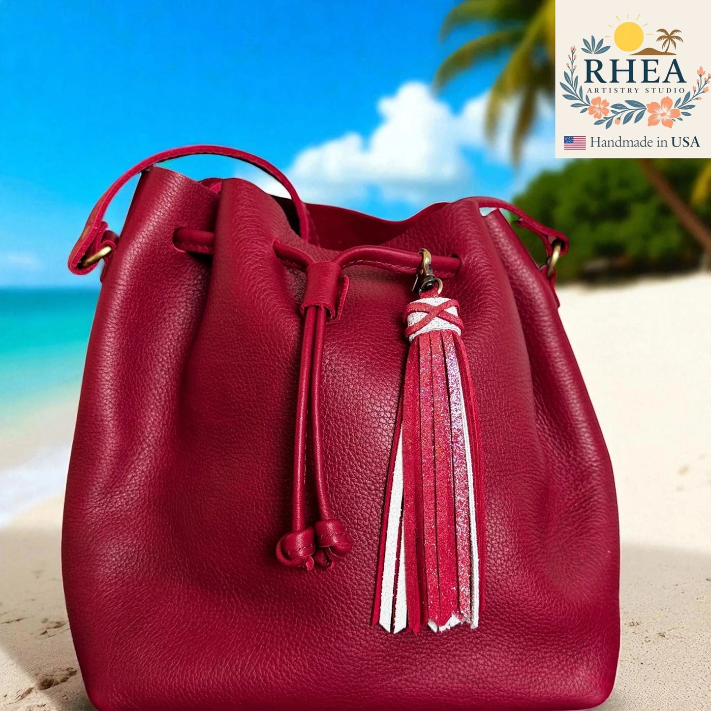 Red leather bucket bag with tassel on a beach background, featuring RHEA brand.