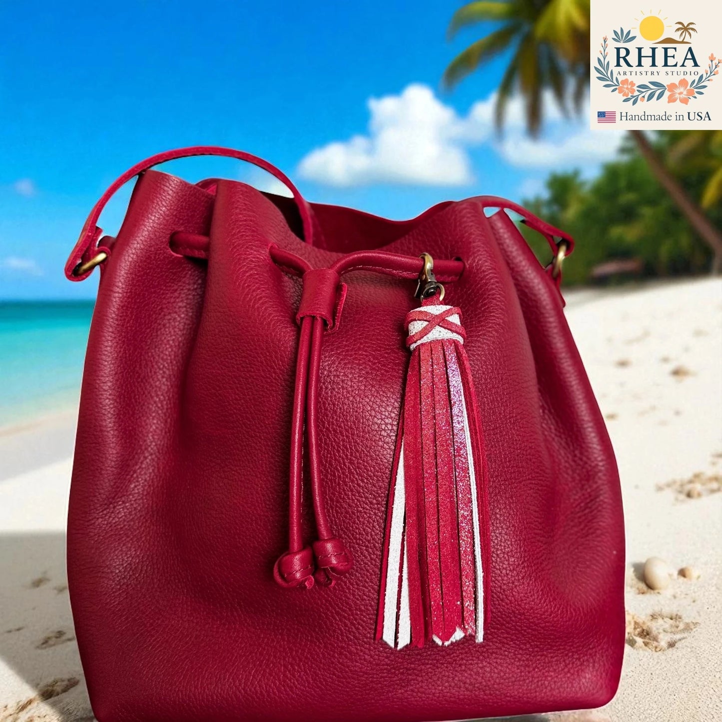 Red leather bucket bag with tassel on a beach background, featuring the RHEA brand.