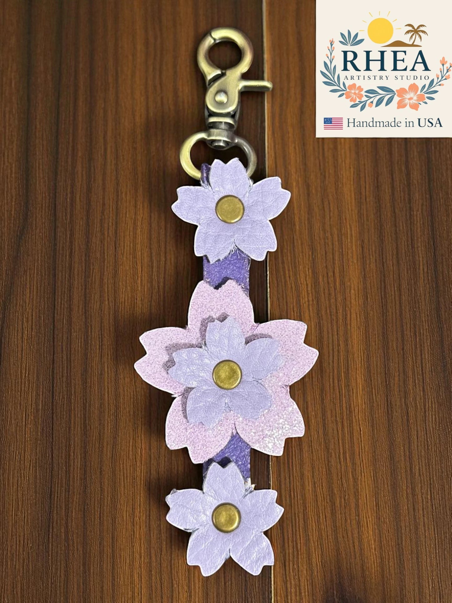 handmade leather bag charm lavender accents on a wooden background, featuring the RHEA Artists Studio logo.