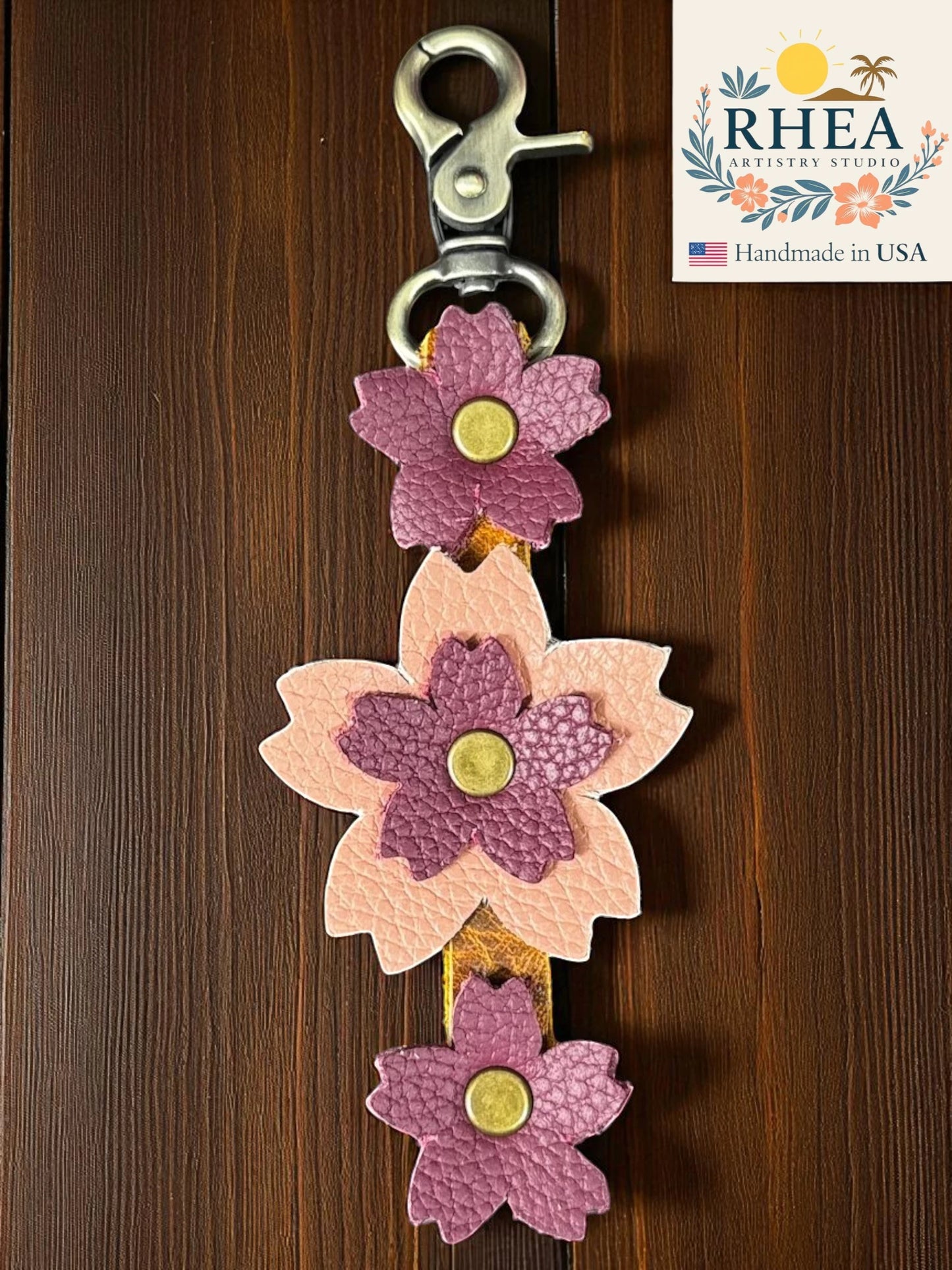 handmade leather bag charm with peach plum colors on a wooden surface, featuring the RHEA brand.