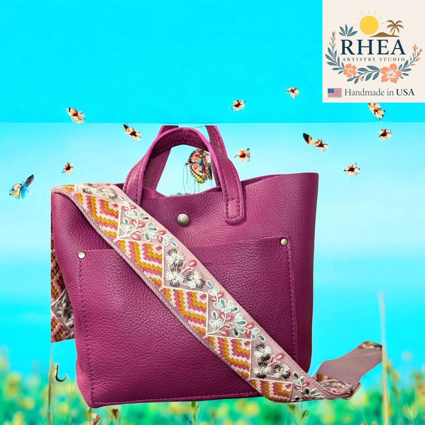 Purple handbag with an embroidered strap on a blue background, featuring the RHEA brand.