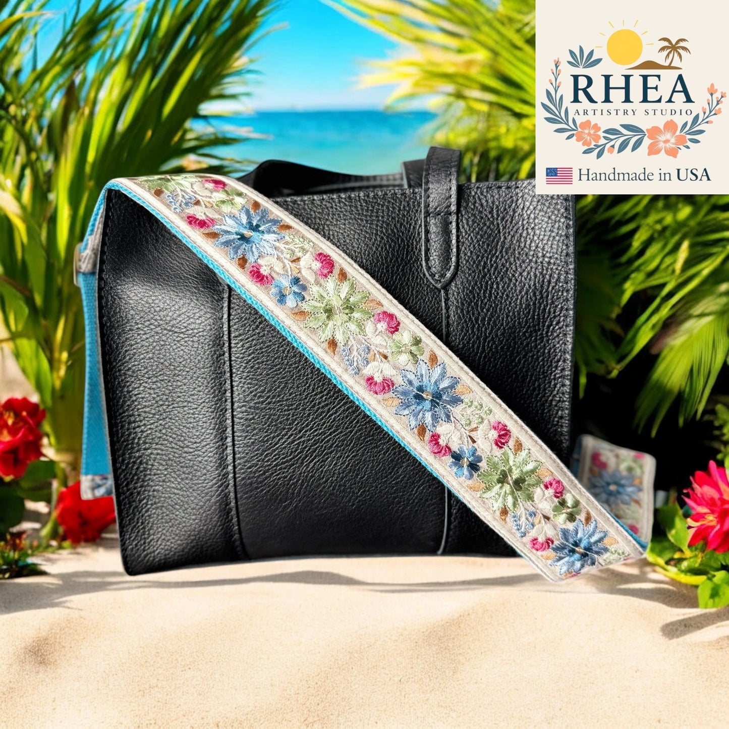 Black handbag with a floral purse strap on a sandy background with plants and flowers.