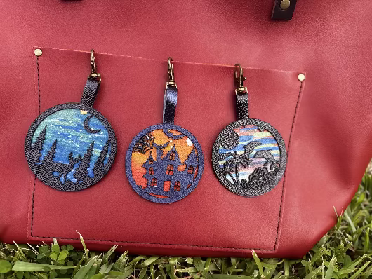 A handpainted leather charm with a halloweendesign, attached to a black leather bag.