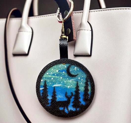 Round keychain with bear and moon design hanging from a white handbag.