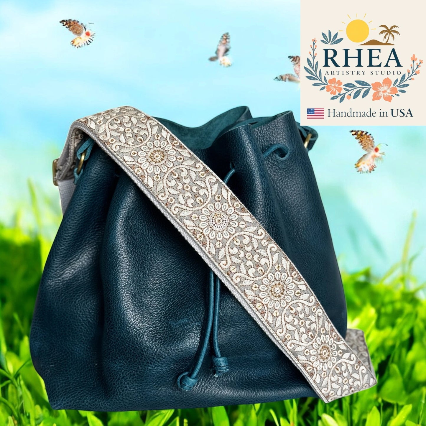 Blue leather bag with a decorative purse strap on a grassy background, featuring RHEA Artistry Studio logo.