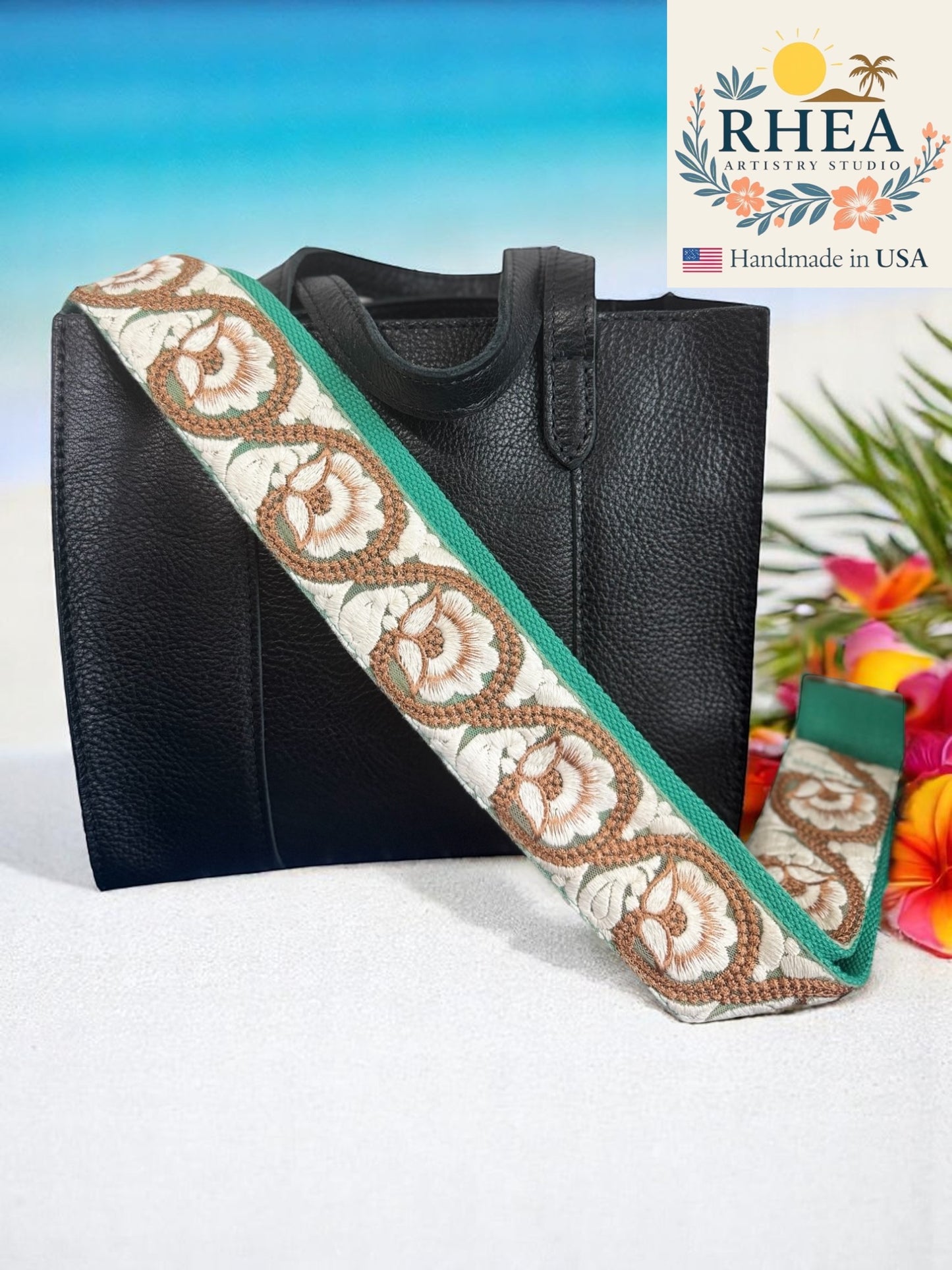 Black handbag with a decorative purse strap featuring floral patterns on a white background, with 'RHEA Artisan Studio' branding.