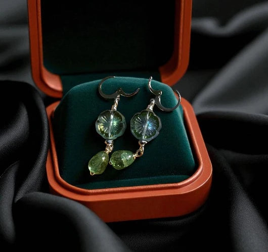Green gemstone earrings in a jewelry box on black fabric