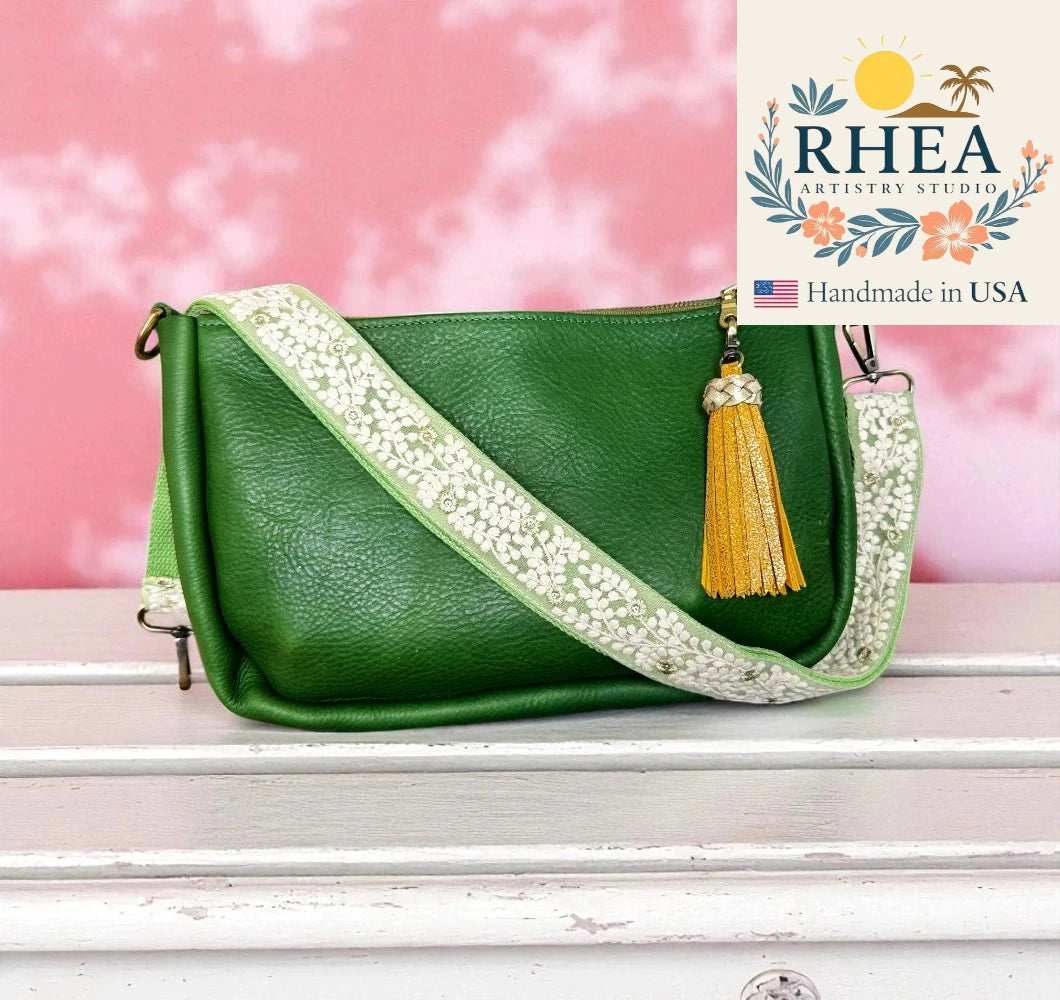 Green handbag with decorative strap and tassel on a pink background, featuring RHEA Artistry Studio logo.