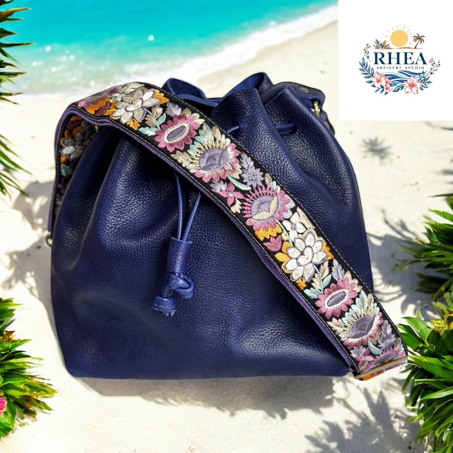 Lavender and yellow embroidered sunflower strap on black webbing, attached to navy leather bucket bag on beach