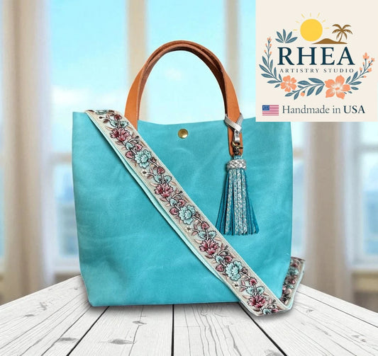 Turquoise handbag with a decorative strap and tassel, featuring the RHEA Artistry Studio logo.