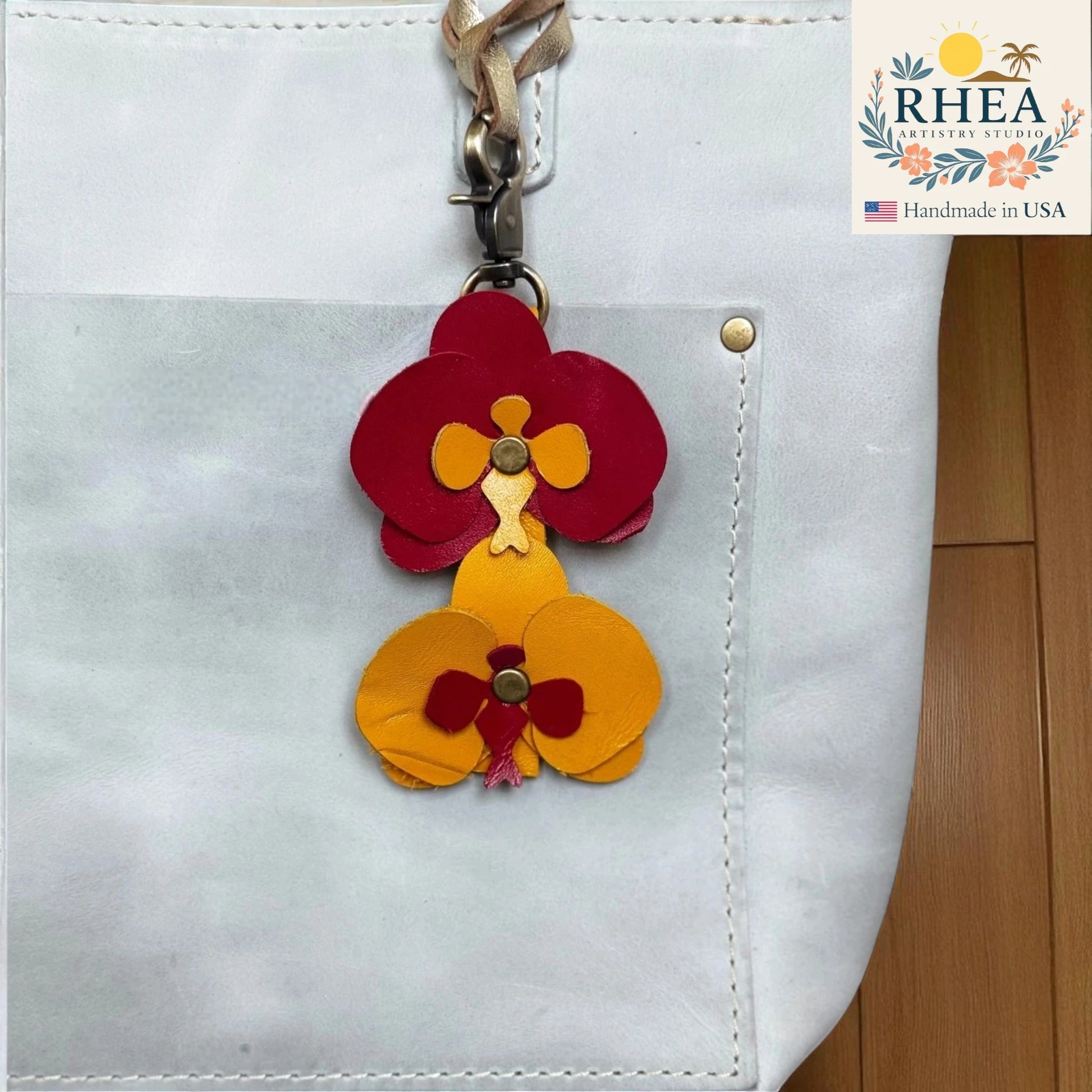 Floral leather bag charm attached to a white bag with RHEA Artistry Studio branding.