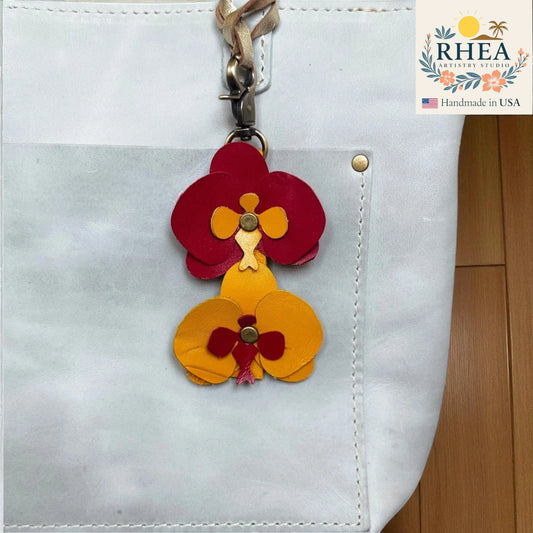 Floral leather bag charm attached to a white bag with RHEA Artistry Studio branding.