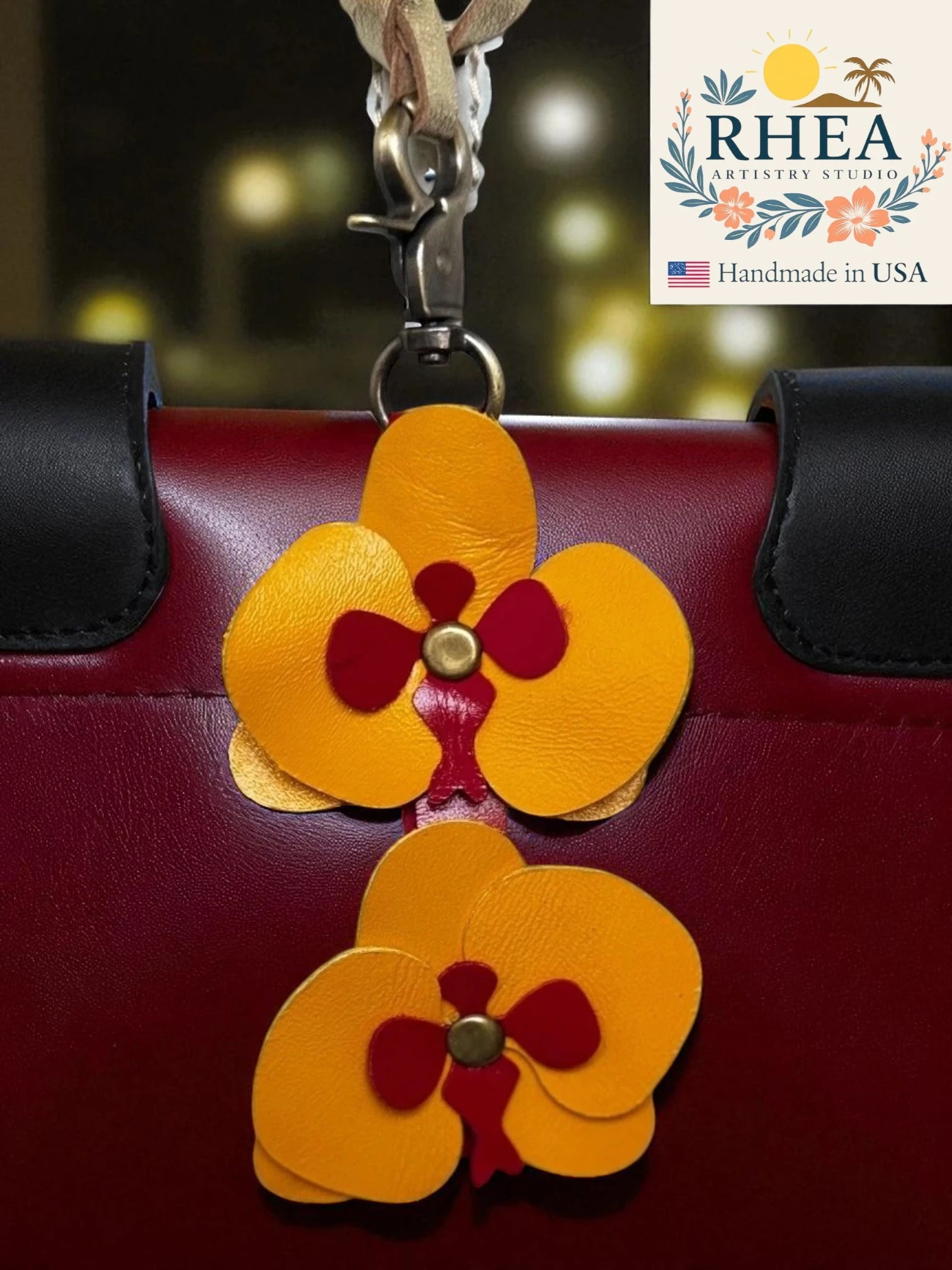 Red handbag with yellow flower-shaped leather bag charm and RHEA branding.