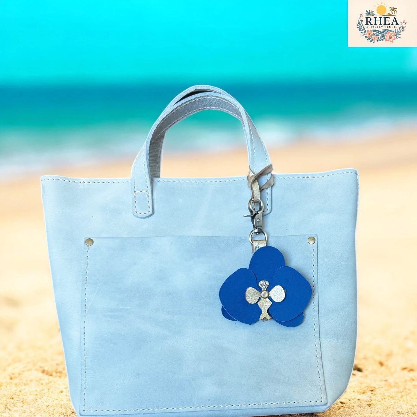 Light blue handbag with a blue flower charm on a beach background
