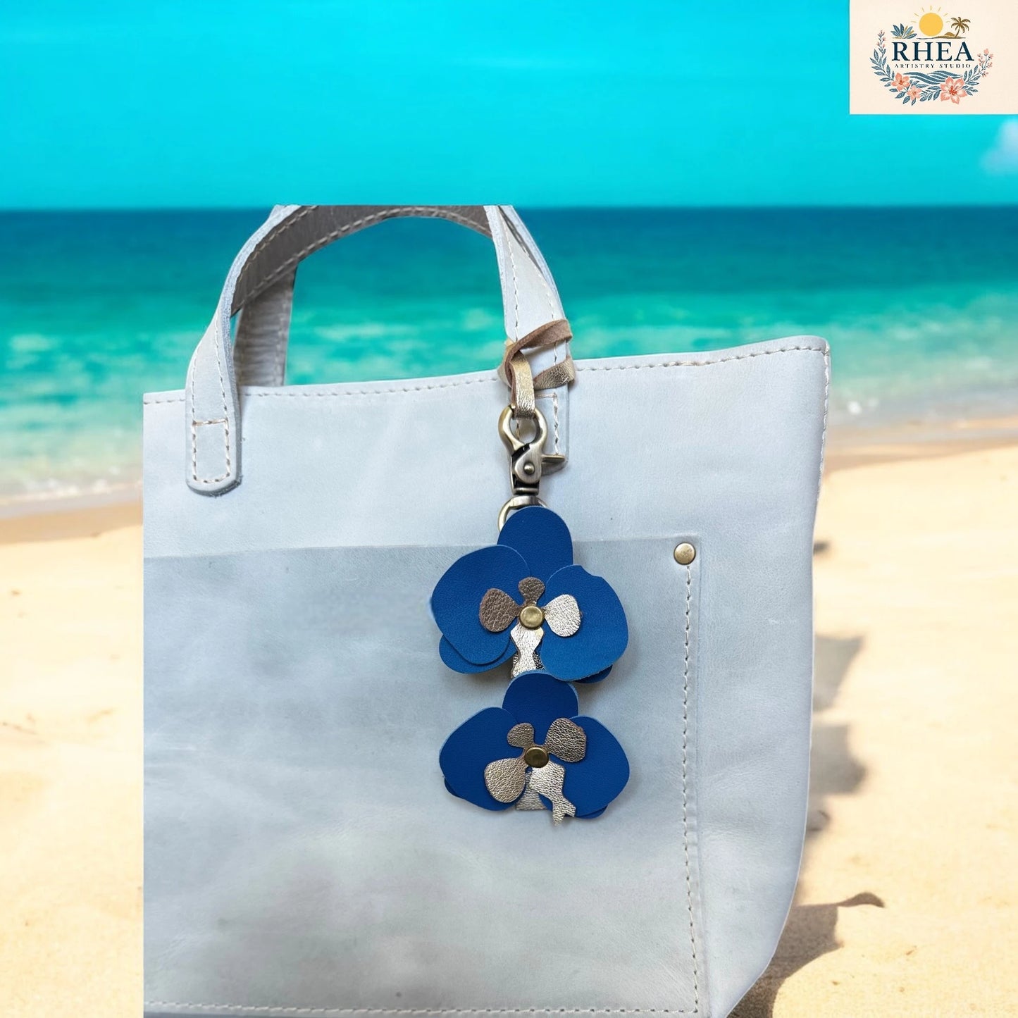 Light blue tote bag with blue flower keychain on a beach