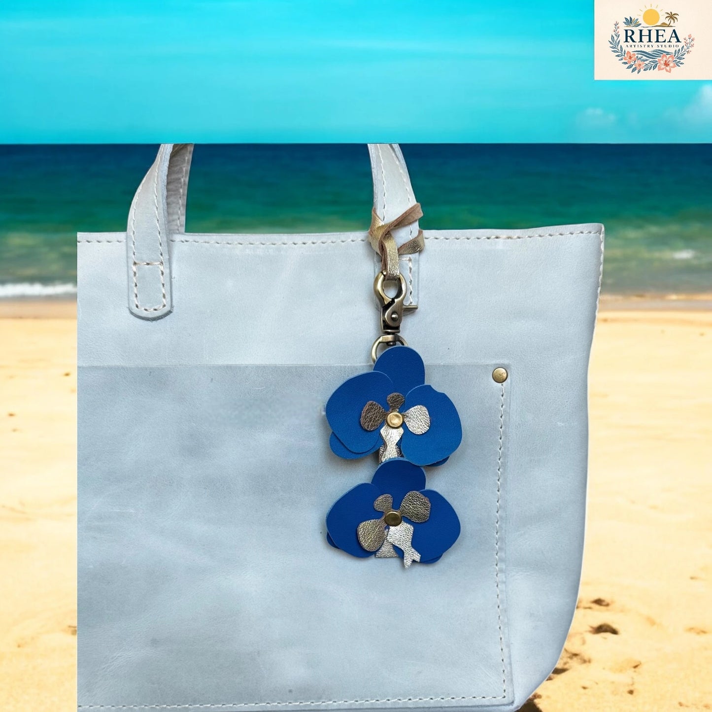 Light blue tote bag with a blue flower charm on a beach background