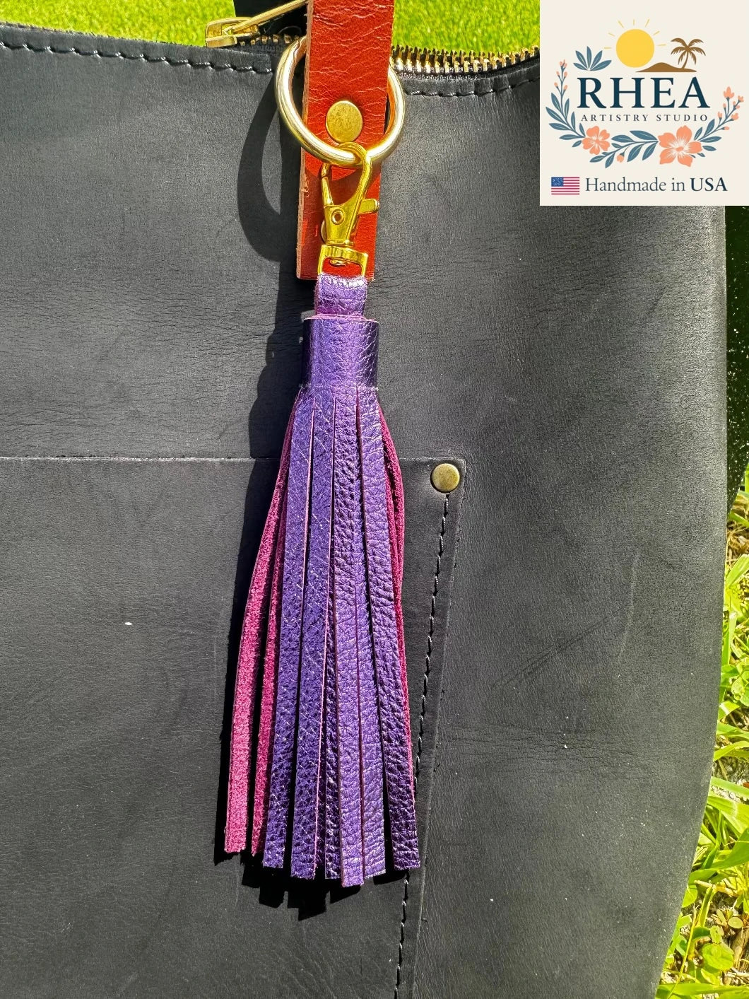 Purple tassel on a black leather bag with RHEA Artisan Studio branding.