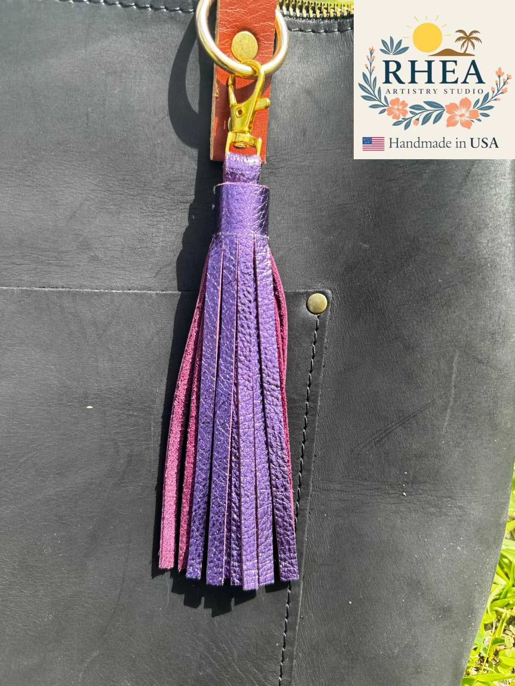 Purple leather tassel on a black leather bag with RHEA branding.