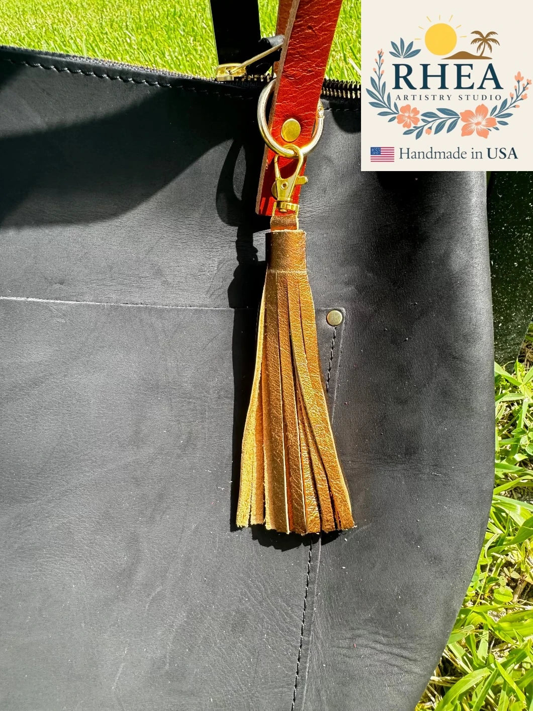 bronze Leather tassel on a gray bag with RHEA branding in the corner.