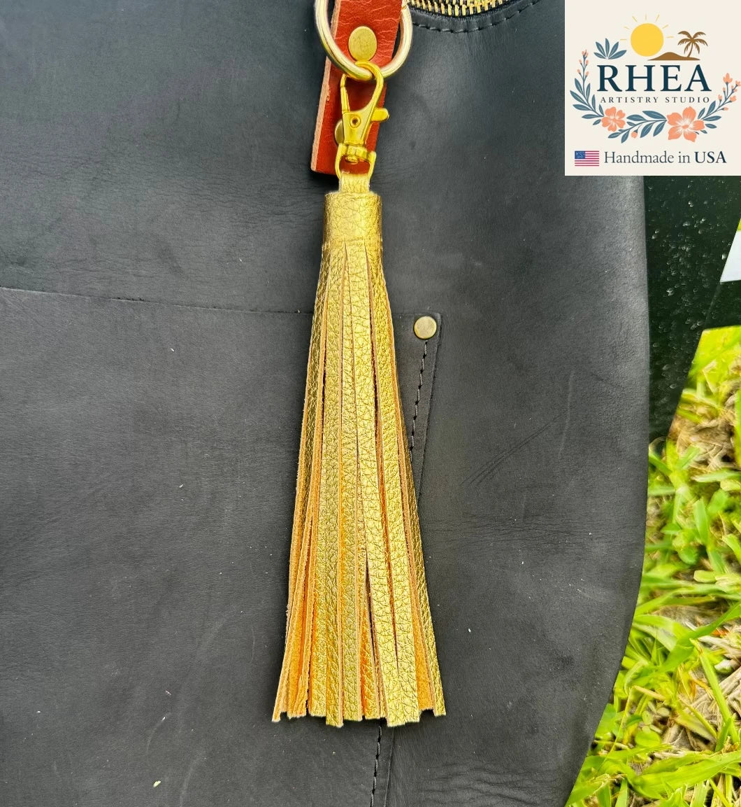 Yellow tassel on a black leather bag with RHEA Artistry Studio branding.