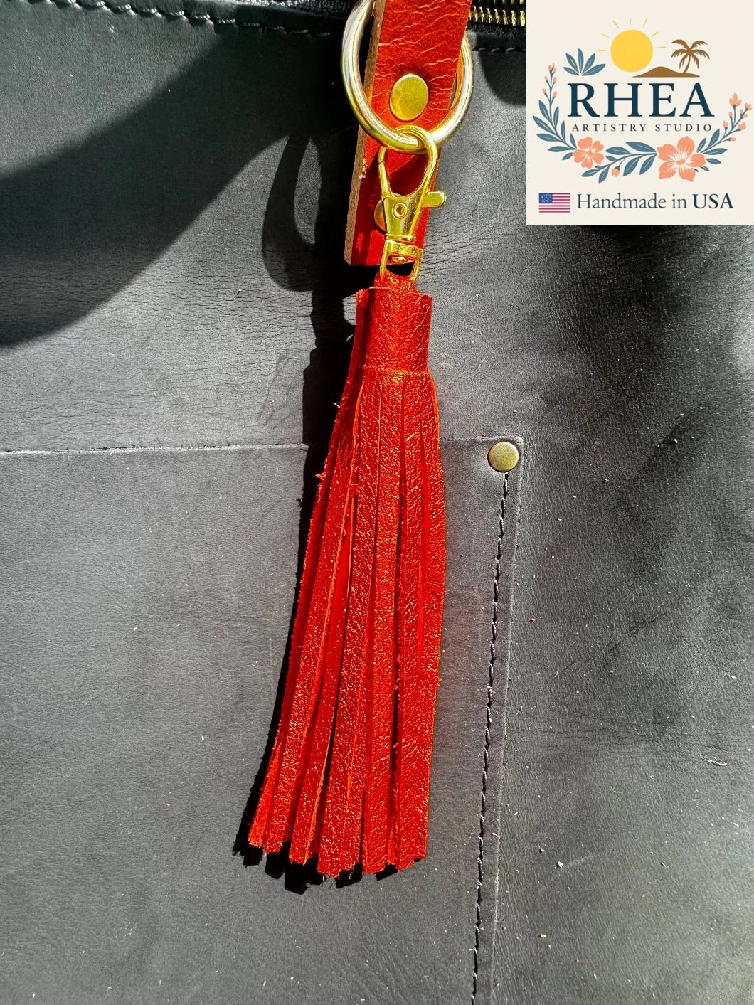 orange tassel on a black leather bag with RHEA Artistry Studio logo.