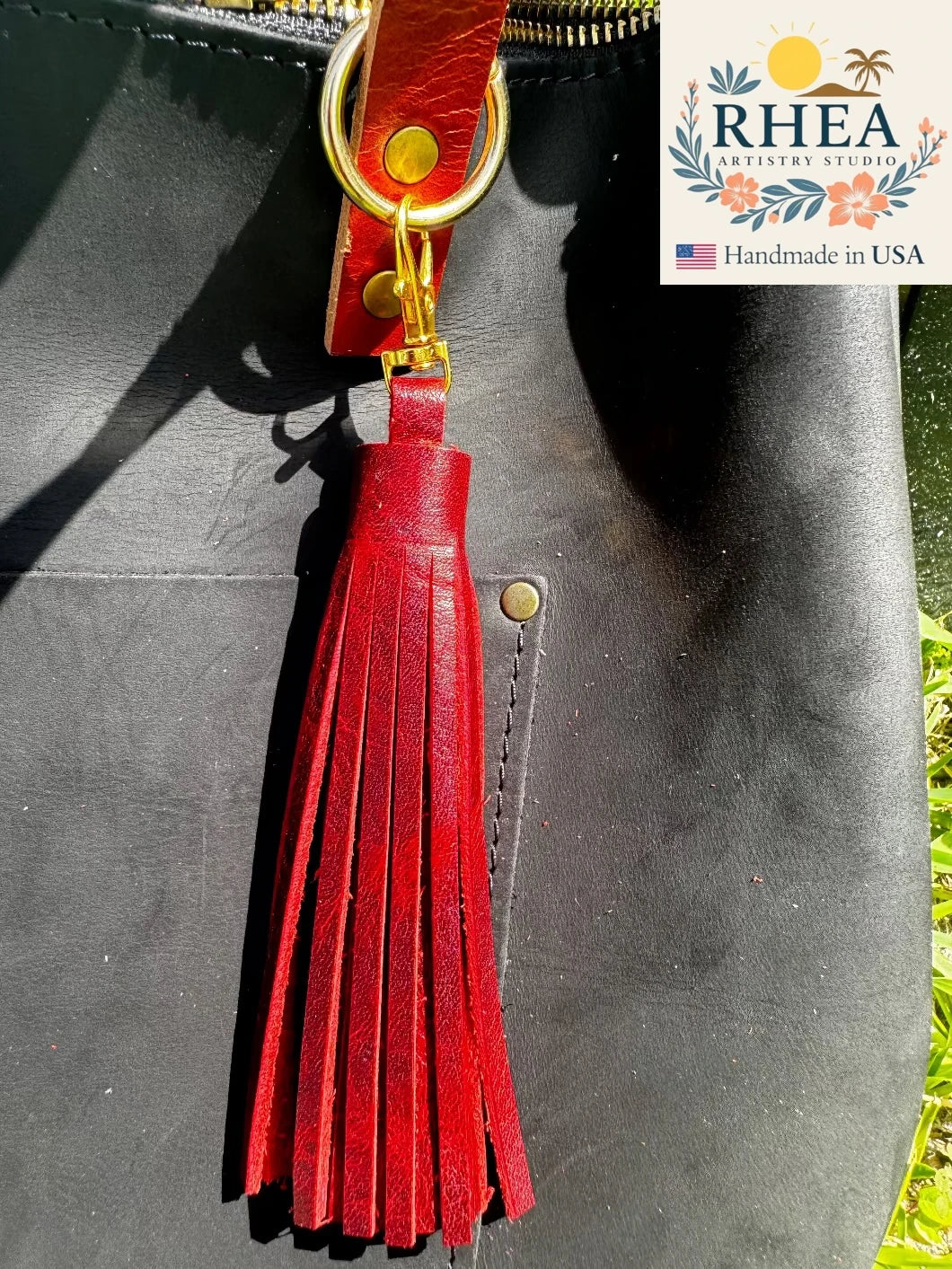 sangria leather tassel on a black bag with RHEA logo in the corner.