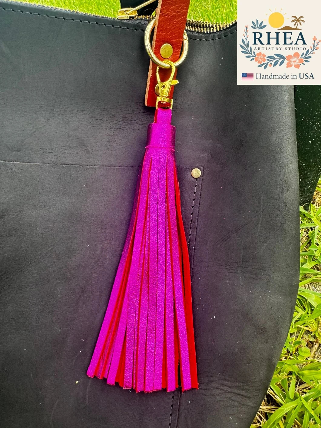 Black leather bag with a pink tassel keychain, RHEA brand visible.