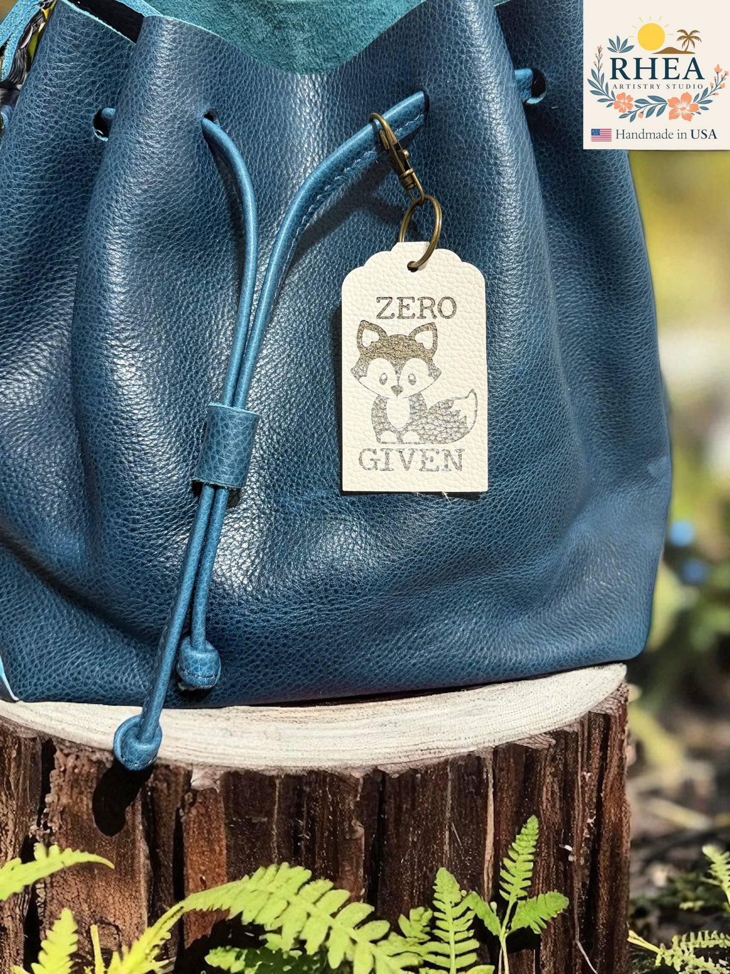 Blue leather bag with a 'ZERO GIVEN' tag on a wooden stump with greenery
