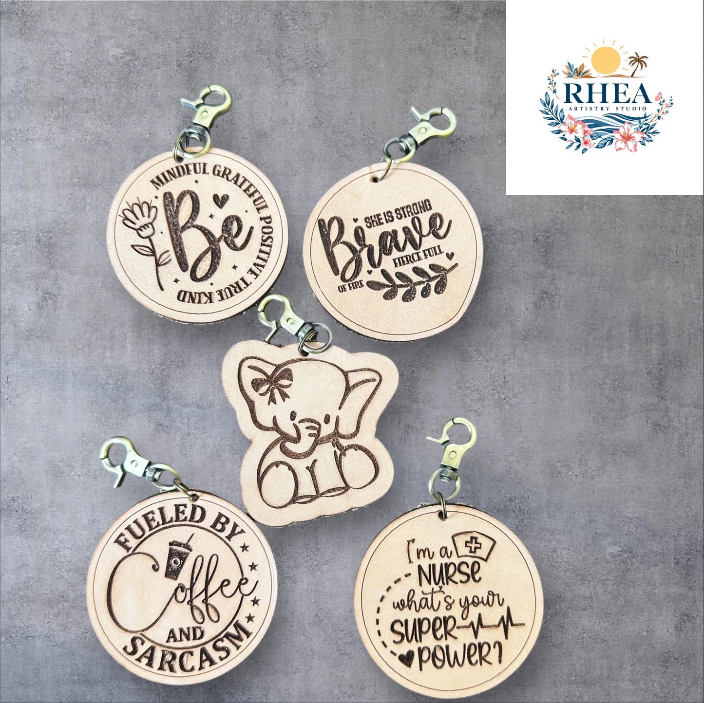 Five wooden keychains with engraved text on a gray background, featuring the brand 'RHEA'.
