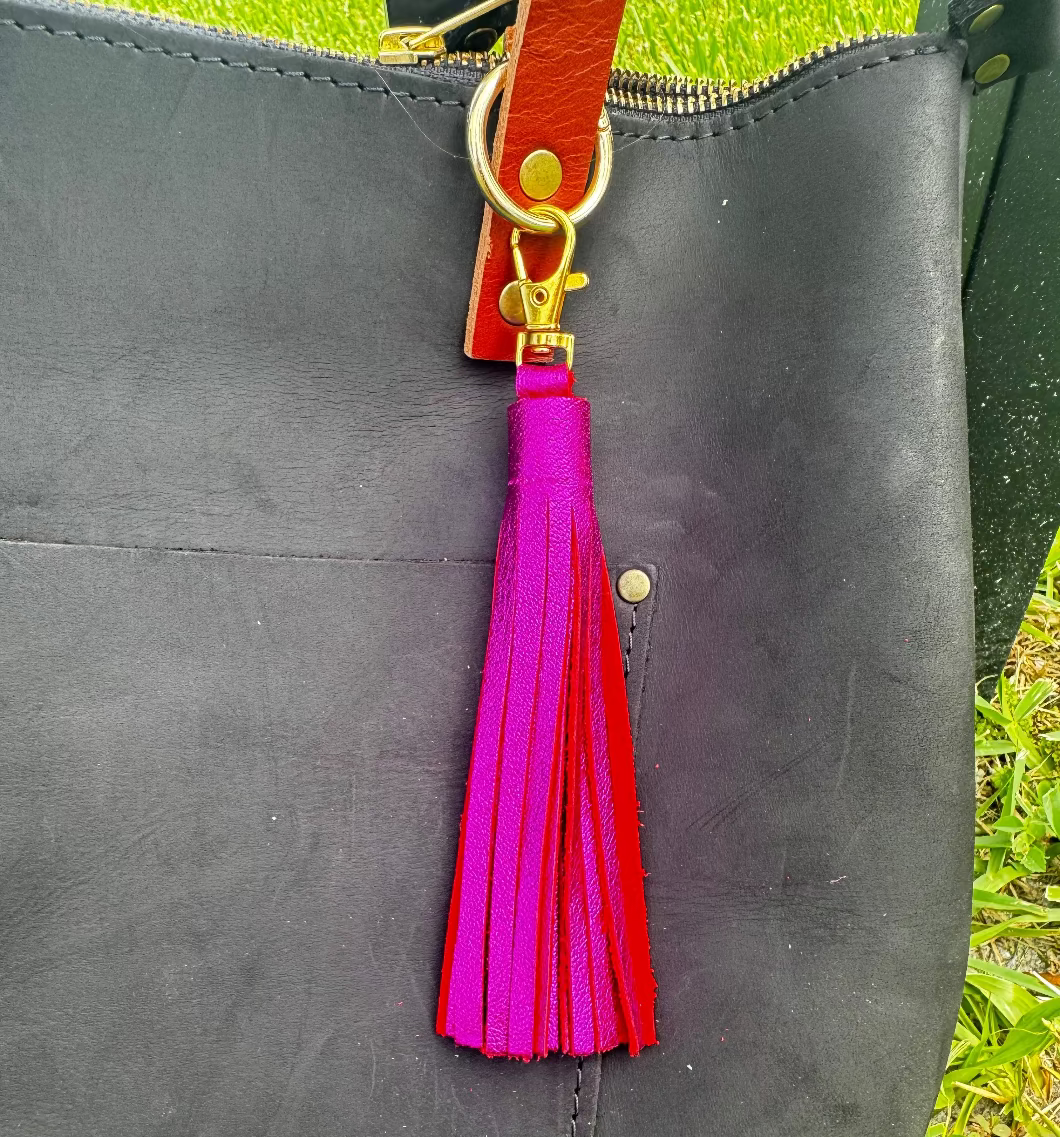 A jumbo leather tassel accessory in hot pink color, displayed on a black handbag with a red strap.