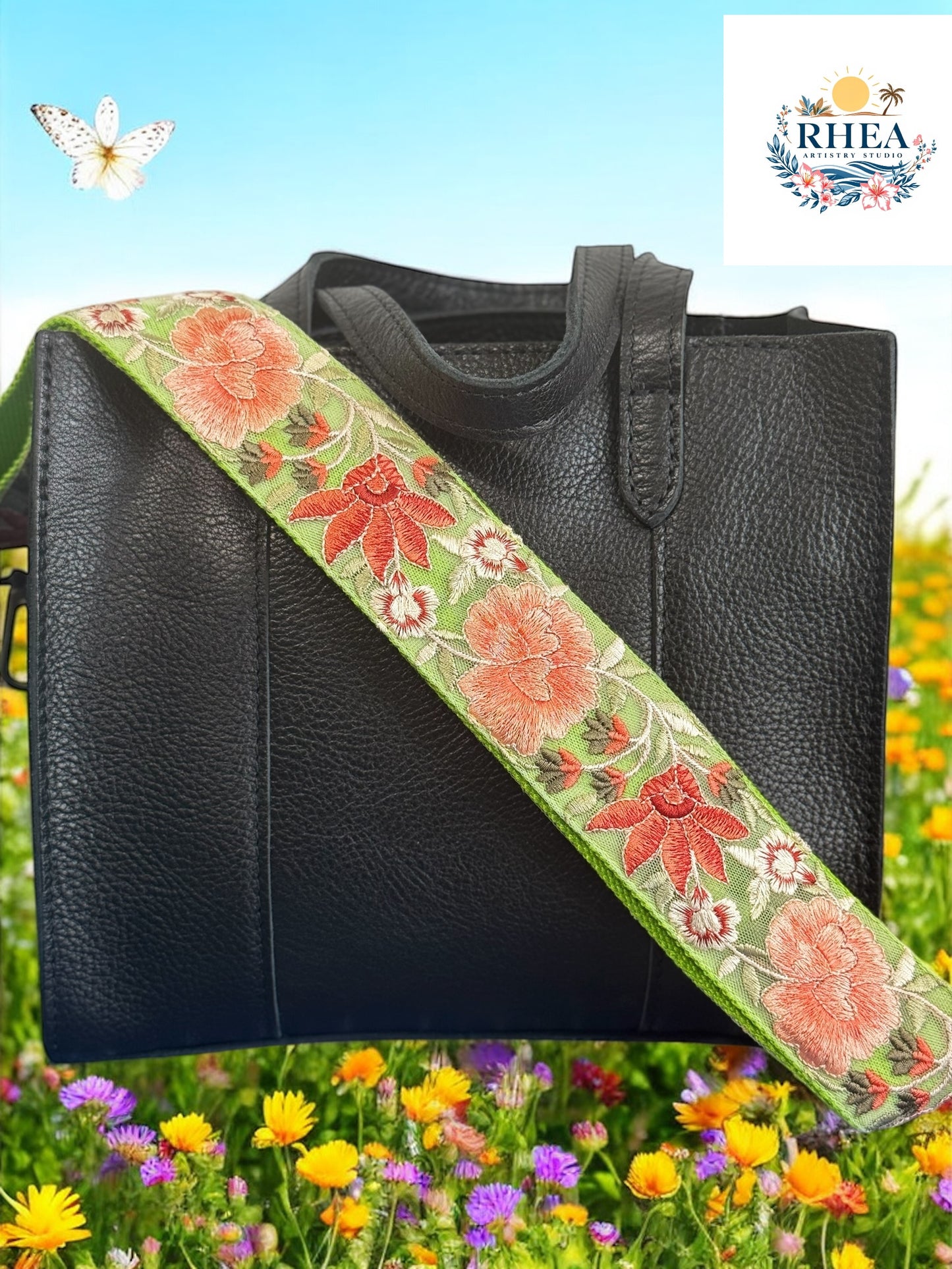 A black purse with a pink and green floral embroidered strap placed on a surface with a field of flowers in the background.