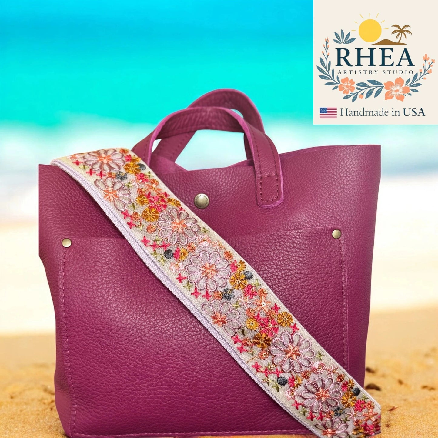 Purple handbag with a floral strap on a beach background, featuring the RHEA Artisan Studio logo.