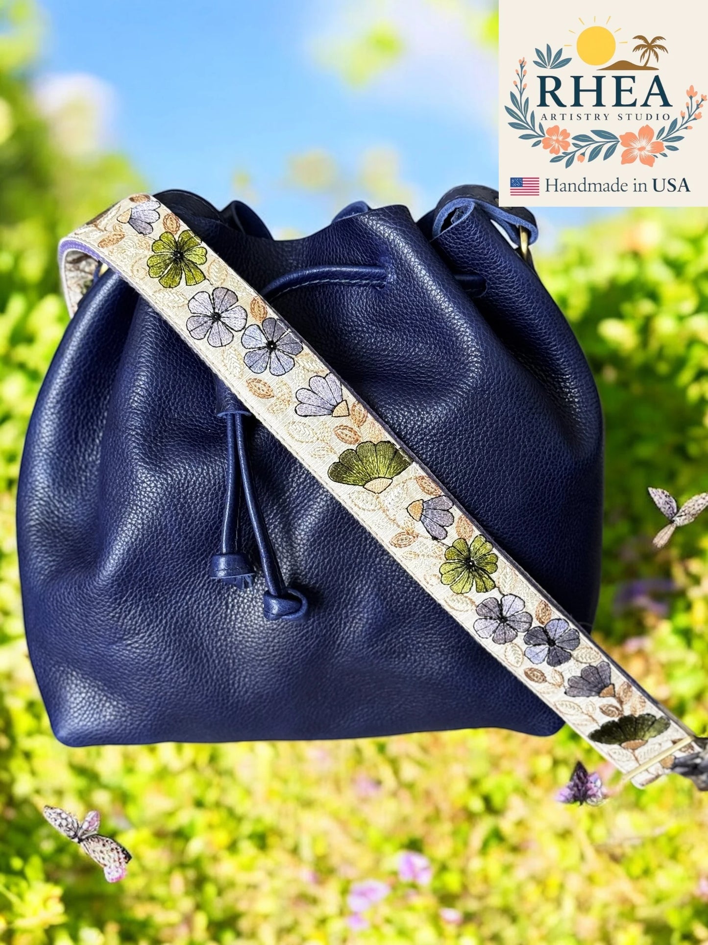 Navy blue leather bag with floral purse strap against a blurred natural background