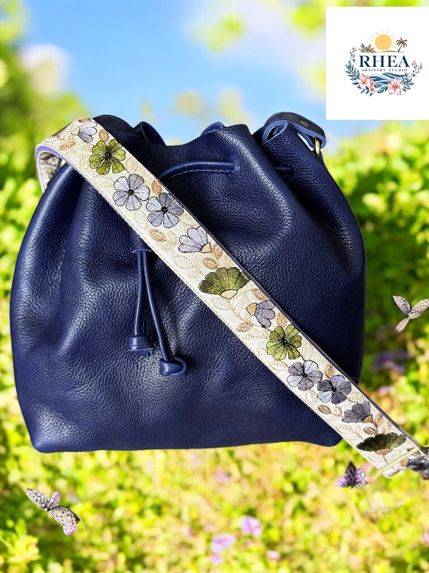 Navy leather bucket bag with a cream strap detailed in violet, sage, and charcoal floral motifs.