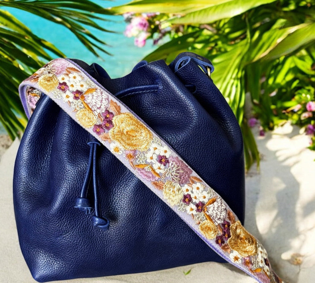 Navy blue bucket bag with lilac-embroidered wide strap featuring yellow poppies and plum accents by Rhea Artistry Studio.