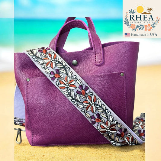 Purple handbag with an embroidered purse strap on a beach background, featuring the RHEA brand.