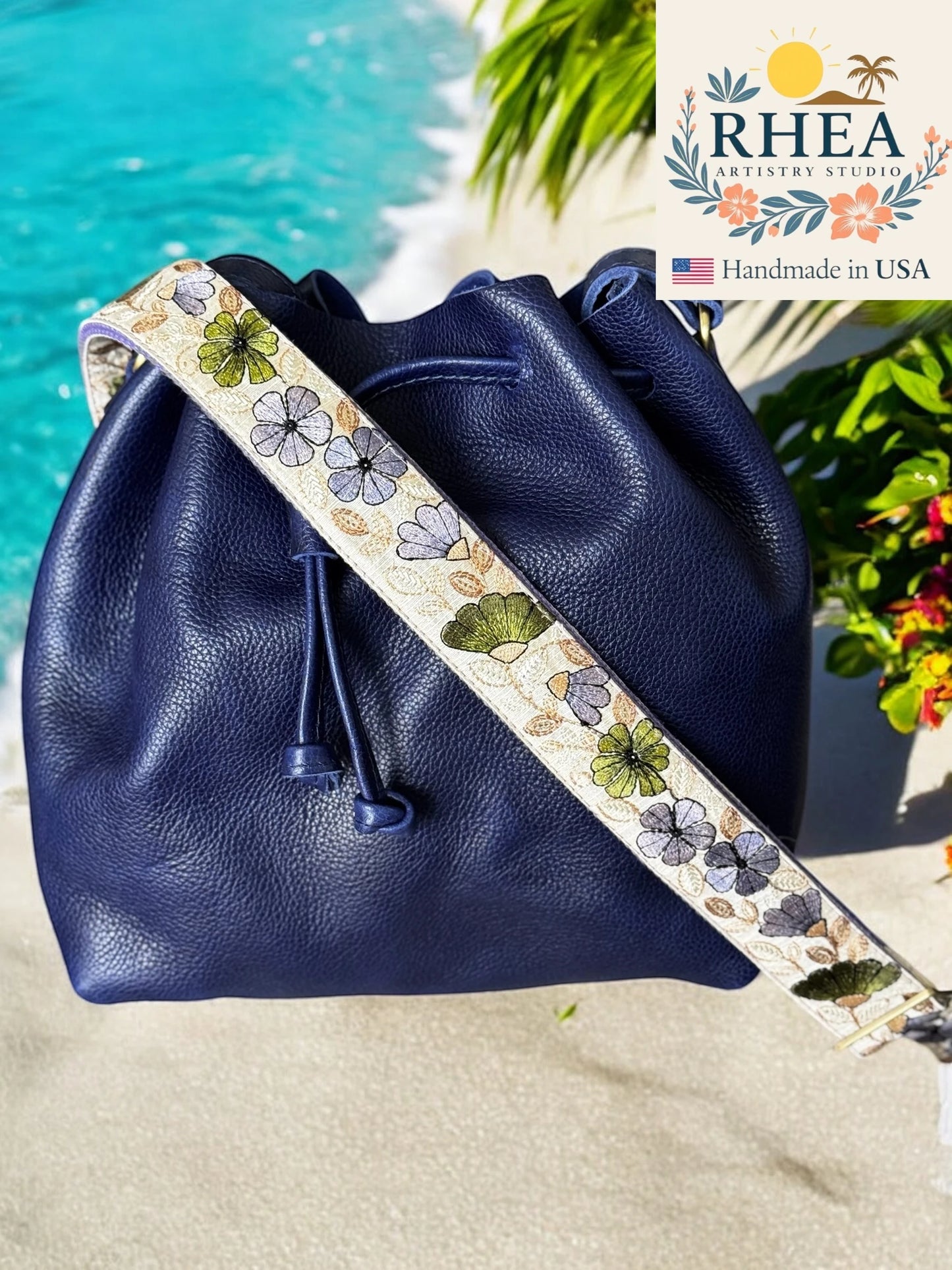 Navy blue leather drawstring bag with floral purse strap by RHEA, handmade in USA, by a poolside.