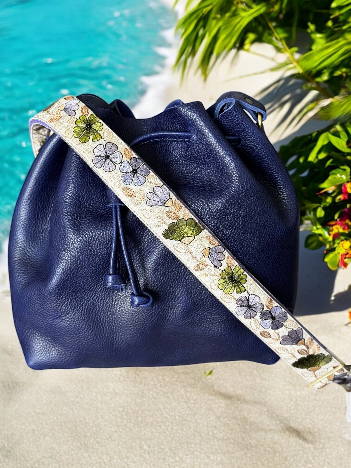 Navy leather bucket bag with a cream strap detailed in violet, sage, and charcoal floral motifs.