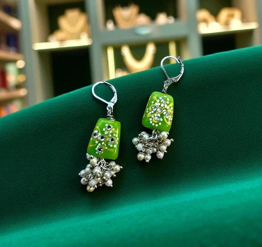 Green earrings with pearl-like beads on a green surface