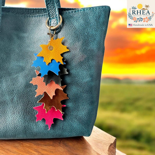 Colorful maple leaf-shaped leather purse charm on a blue bag with a sunset background