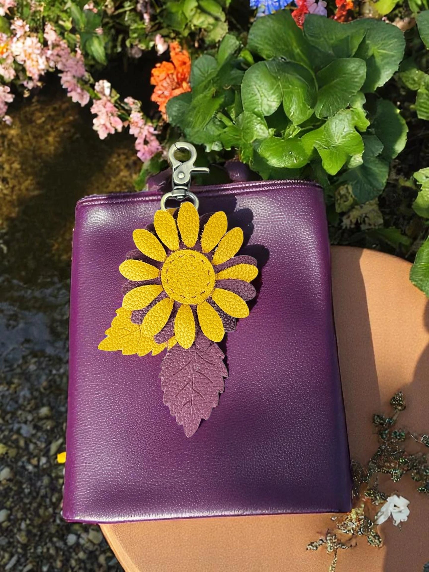 Hand-sewn leather daisy charm in marigold and plum with brass clasp and textured leaves in the garden