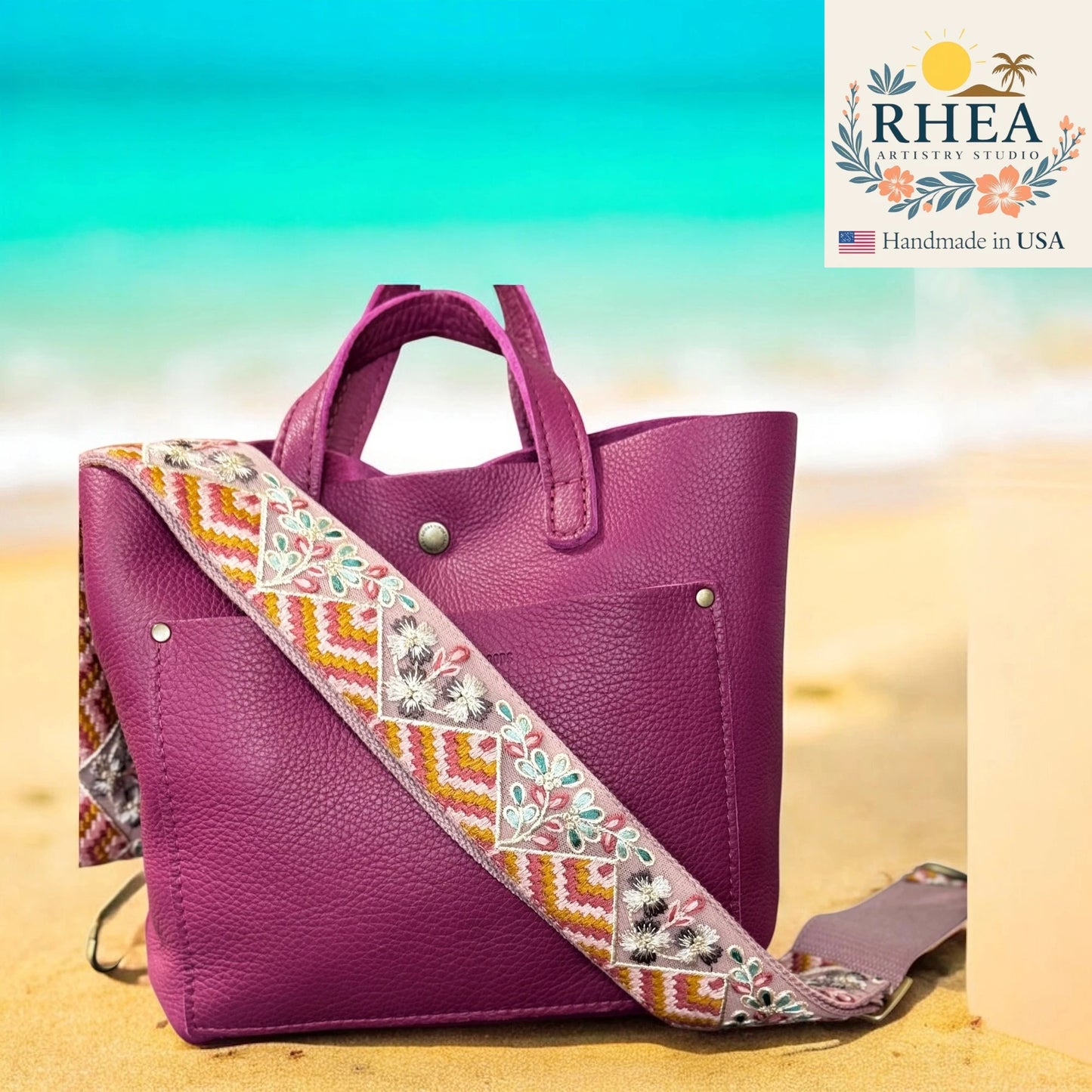 Purple handbag with an embroidered strap on a beach background, featuring the RHEA brand.